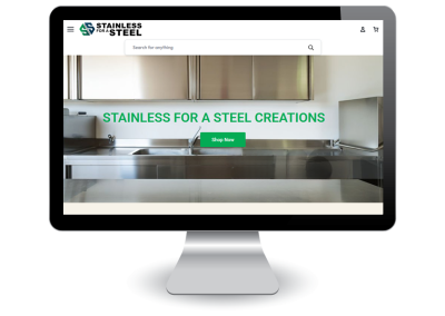 A computer monitor displays a website with a stainless steel kitchen background, featuring the text STAINLESS FOR A STEEL CREATIONS and a green Shop Now button. The website logo is at the top left.